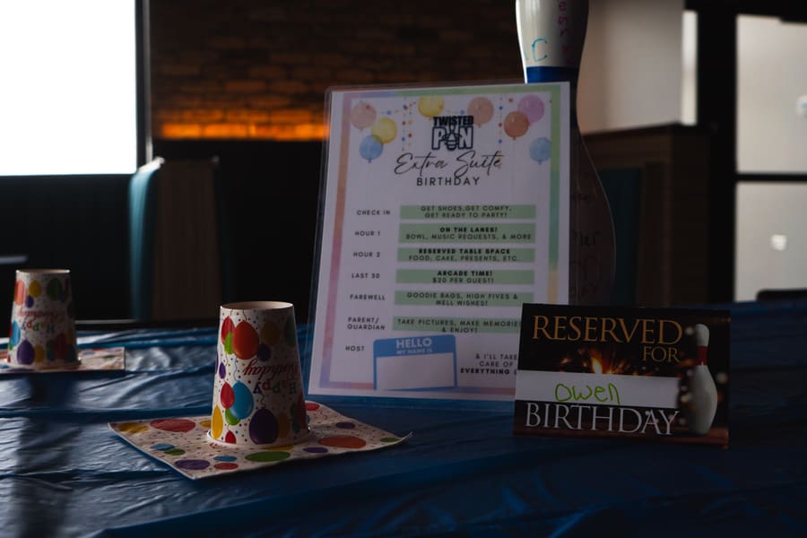 A Twisted Pin kids' birthday party set up — table with Extra Suite Birthday placard, balloon-print party cups, and a reserved-for sign with a bowling pin
