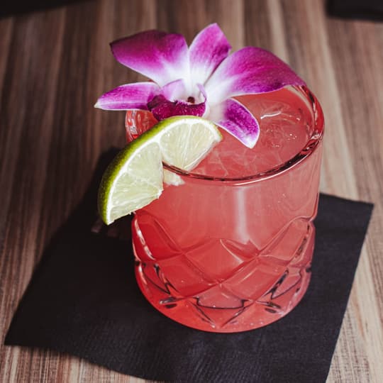 A pink craft cocktail with an orchid and lime garnish at Twisted Pin