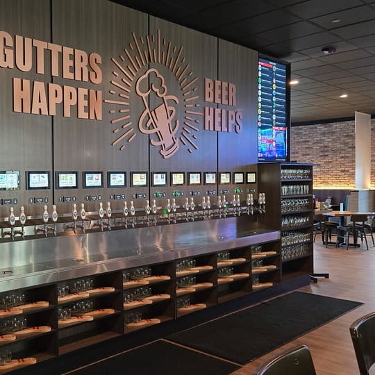 The 28-tap self-serve beer wall at Twisted Pin with the GUTTERS HAPPEN BEER HELPS sign